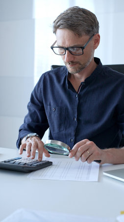 Businessman working in office using calculator and magnifying glass analyzing financial documents,...