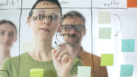 Professional businesswoman wearing glasses writing on glass board, marking strategic plan with...