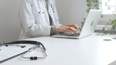 Stethoscope over a medical records are lying on the desk opposite the doctor is typing on a laptop with a in a medical office, suggesting online healthcare or telemedicine services. Medicine conceptの写真素材