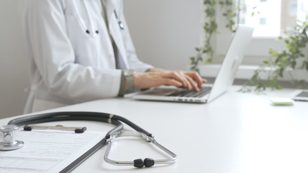 Stethoscope over a medical records are lying on the desk opposite the doctor is typing on a laptop with a in a medical office, suggesting online healthcare or telemedicine services. Medicine conceptの写真素材