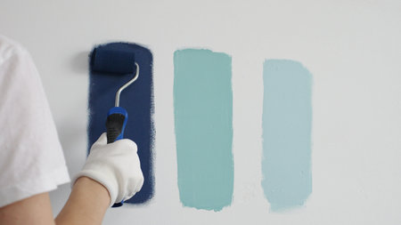 Painter wearing protective gloves rolling blue paint on white wall, creating gradient color effect...