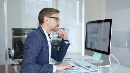 Businessman in a blue jacket analyzing financial data charts on computer, making important business...