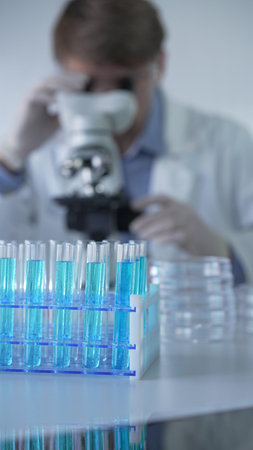 Test tubes with a blue liquid, close-up view. Male scientist wearing white protective gloves and...