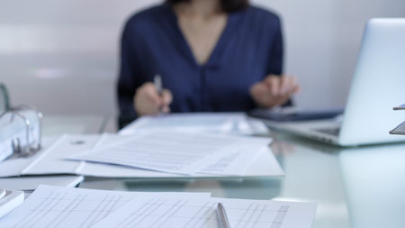Magnifying glass, white calculator, pen and documents are lying on accountants desk. Businesswoman wearing blue dress is working with documents on the background. Business and audit conceptの写真素材