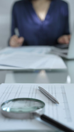 Businesswoman wearing blue dress is working with laptop, calculator and documents in a professional office setting. Low lighting, close-up vertical view. Business people, audit conceptの写真素材