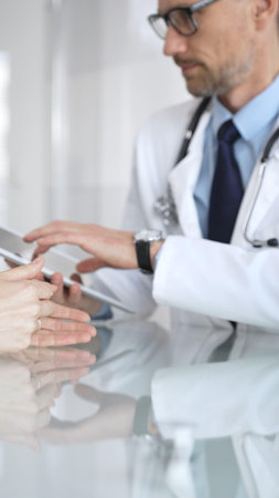Male doctor consulting female patient, discussing diagnosis and medical history with digital tablet in clinic. Medicine and health careの写真素材