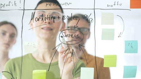 Marketing team collaborating, strategizing business growth with colorful sticky notes on transparent board, targeting revenue and profitability goalsの写真素材