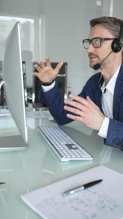 Male call center agent wearing headset providing online customer support, consulting client on...