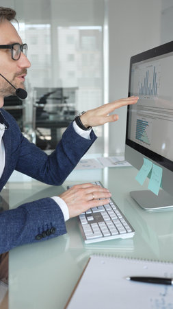 Man in headset talking during online video call, working in office, consulting remote customers, providing technical support. Business people conceptの写真素材