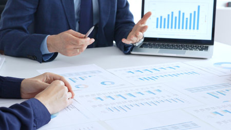 Business people reviewing financial charts and reports in office, using a laptop and calculator...