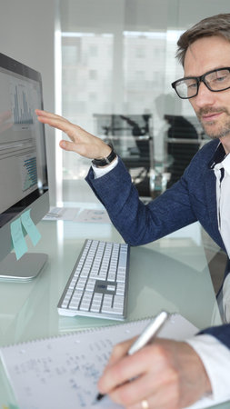 Professional businessman in a blue jacket working on desktop computer in modern office, focusing on his work and business tasks. Business people conceptの写真素材