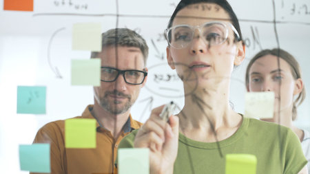 Professional team strategizing, writing collaborative notes on glass board, mapping innovative project workflow with markerの写真素材