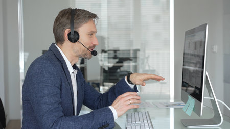 Male call center agent wearing a headset, providing online customer support and consulting clients...