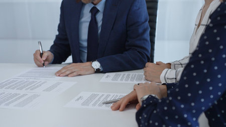 Professional businessman wearing tailored suit signing contract at sleek desk, sealing business...