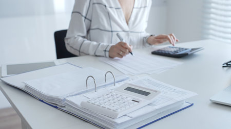 White calculator is on financial documents, with an accountant taking notes, emphasizing accounting, finance, and tax preparation, close up. Audit and taxes conceptの写真素材