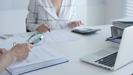 Two professional accountants working together, using a magnifying glass and a calculators, to audit...