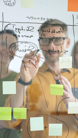 Business people colleagues brainstorming, writing strategy notes on glass board, collaborating with...