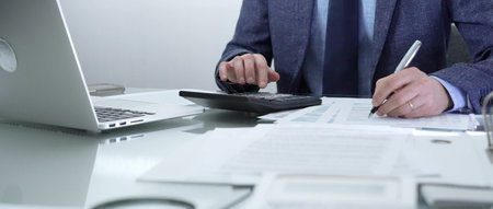 Businessman or accountant wearing blue suit is working with laptop, calculator and documents in...