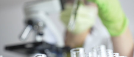 Close up of test tubes with a scientist analyzing plant samples in test tubes with a microscope in a...