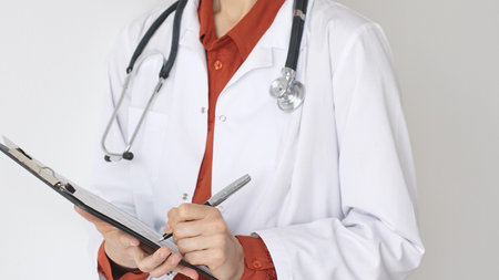 Unknown woman doctor wearing stethoscope and white coat over brick red blouse is standing and...