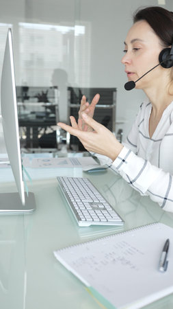 Woman working in call center, providing customer support through headset, communicating in virtual...