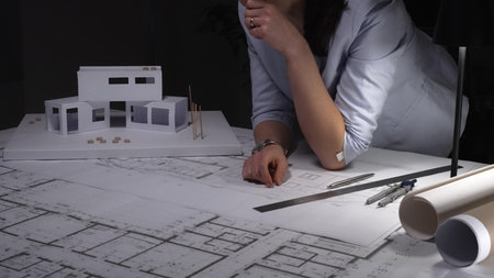 Architect analyzing building plan with house model, developing construction blueprint, designing new...