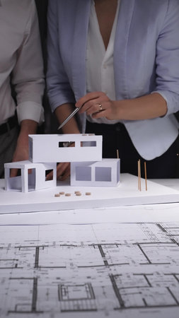 Architects developing a future building project, using architectural plans and a paper model to...