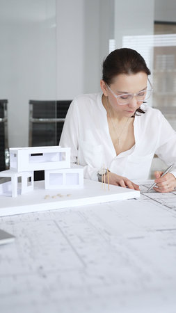 Professional architect woman designing building blueprints in modern office, using laptop for...