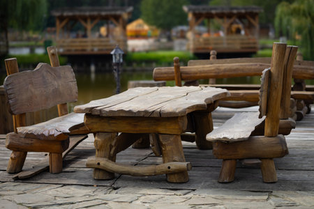 Rustic wooden bench and table set on lakeside patio in a serene park on a calm day. Concept of outdoor seating, nature, and relaxation in a rustic environment surrounded by natural beautyの写真素材