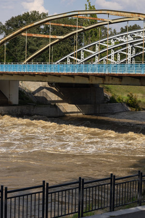 Rushing water flowing under a steel bridge after heavy rainfall, capturing the power of nature and urban infrastructure in flood prevention. Concept of river flooding, stormwater and city resilienceの写真素材