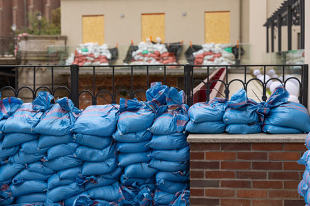 Protective barrier of blue sandbags stacked along building to shield property from flooding and rising waters, emphasizing precautionary measures for flood defense in urban environmentの写真素材