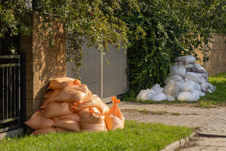 People taking protective measures to safeguard their property during flood season using sandbags as barriers against rising water levels. Flood preparedness and natural disaster responseの写真素材