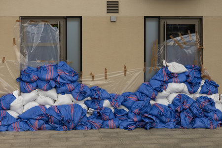 Protective sandbag barrier covers windows of building to prevent flooding damage during high water levels in urban area. Flood protection and emergency preparednessの写真素材