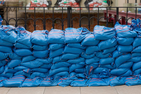 Blue sandbags stacked as a flood barrier along a fence in a European city. Temporary flood...