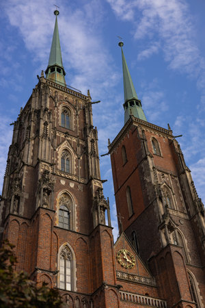 Gothic-style twin spires of Wroclaw Cathedral in Poland under blue sky, showcasing ornate architecture with pointed arches, intricate statues, and a classic clockの写真素材