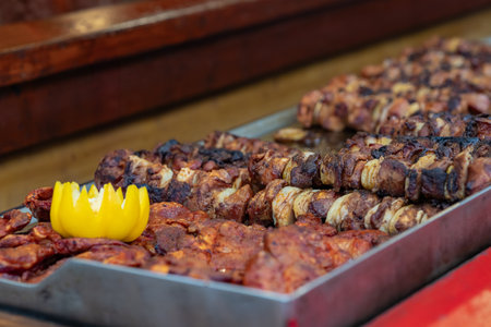 Close-up of grilled skewers and marinated meat on a tray with a decorative yellow bell pepper flower at the Wroclaw Christmas Market. Festive street food, culinary traditions and holiday flavorsの写真素材