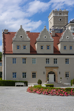 Charming historic building with decorative gables, arched doorway, blooming pink roses in the garden, and cobblestone yard on a sunny day. Classic architecture, elegance and heritage tourismの写真素材