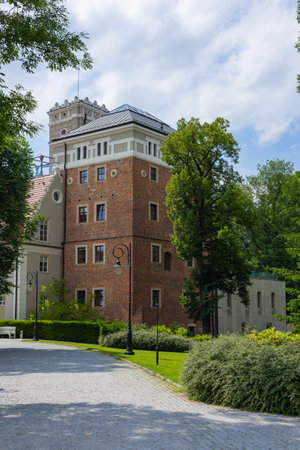 Historic brick building with a modern architectural addition surrounded by lush greenery and cobblestone paths on a sunny day. Architectural contrast, cultural heritage and urban beautyの写真素材