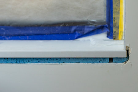 Close-up of a window sill under construction with visible layers of blue insulating foam and protective blue tape. Modern insulation techniques and interior renovation processesの写真素材