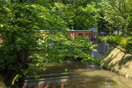Scenic view of a peaceful park with lush green trees, a small canal with a brick bridge with ornate metal railings surrounded by nature, evoking serenity and tranquilityの写真素材