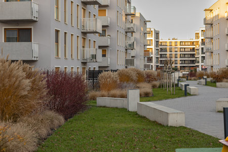 Modern residential courtyard with ornamental grasses, shrubs, young trees and walkways surrounded by contemporary apartment buildings. Urban landscaping, eco-friendly design and sustainable livingの写真素材