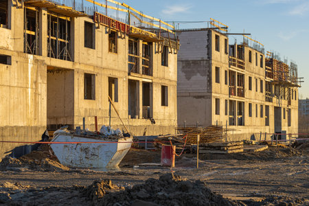Construction site of modern residential buildings under development at sunset with scaffolding, construction materials, and equipment in foreground, reflecting progress and urban infrastructure growthの写真素材