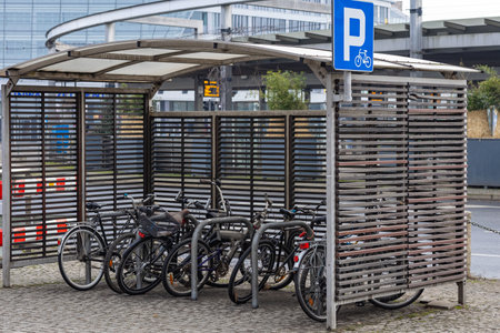 Bicycle parking shelter with multiple bikes locked to metal racks near a modern urban transport hub on a cloudy day. Eco-friendly transport, urban cycling and mobilityの写真素材