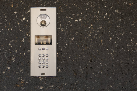 Modern intercom system with numeric keypad, speaker, and camera installed on dark textured stone wall. Secure access control device for residential or commercial buildings, safety and communicationの写真素材