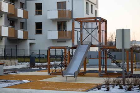 Modern playground with wooden and metal climbing structures, slide, and rope ladders in a residential area. Urban family life, outdoor activities, safe play and child-friendly spacesの写真素材