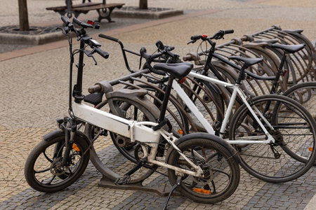 Urban electric and classic bicycles parked in vintage metal bike rack on cobblestone street in city center on cloudy day. Eco-friendly transport, sustainable commuting and urban lifestyleの写真素材