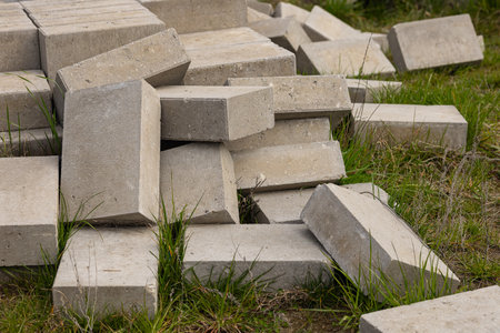 Concrete blocks placed on green grass in urban outdoor setting, symbolizing contrast between construction and nature, with focus on eco-friendly materials, recycling, and sustainable developmentの写真素材