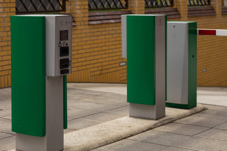 Modern automated access control system with green ticket machine and barrier gate at the entrance of...