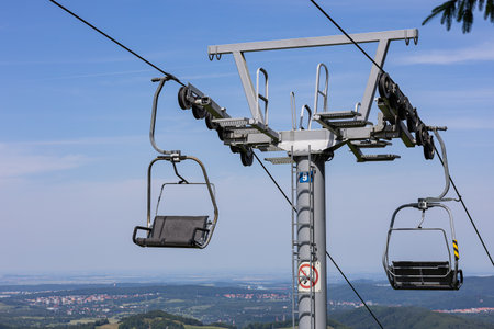 Close-up view of ski lift chair mechanism with cable support tower and pulley system on sunny day. Mountain transport infrastructure, technical engineering and aerial lift operation in summerの写真素材