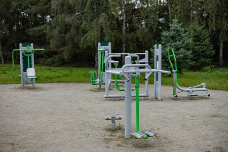 Outdoor fitness equipment is set in a park, showcasing various machines in green and gray, surrounded by trees and grass, encouraging active lifestyle choicesの写真素材